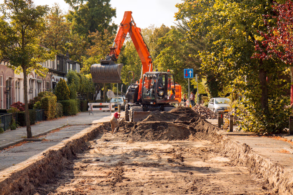 Excavator digging a trench on a residential street for sewer work