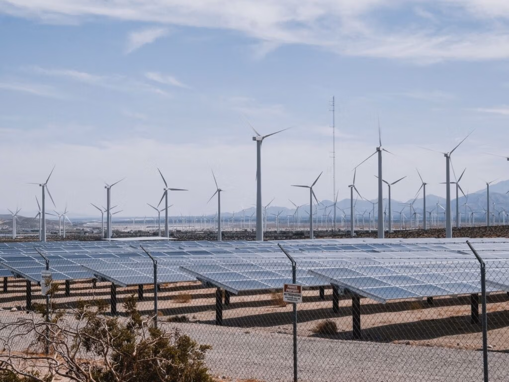 Wind turbines standing behind rows of solar panels in a green field