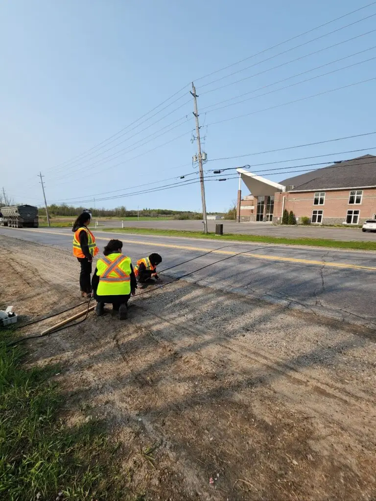 Crew in safety vests setting up a traffic counter at the roadside, Leeds and Grenville