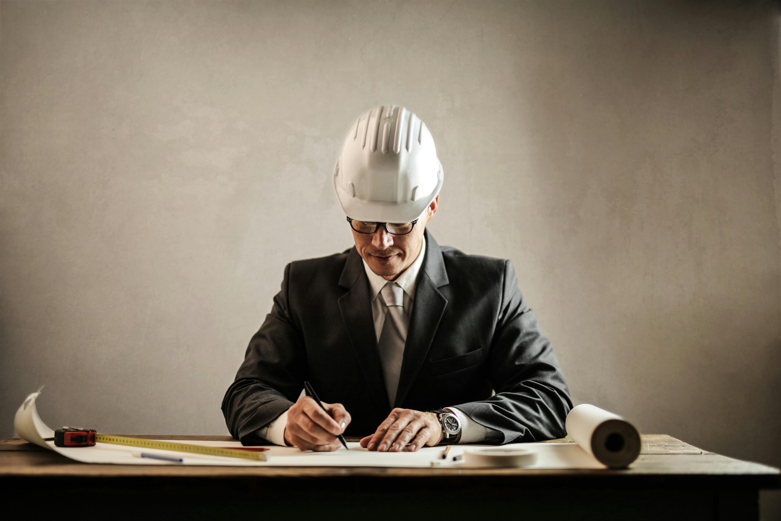 Engineer in a suit drafting architectural plans at a desk indoors.