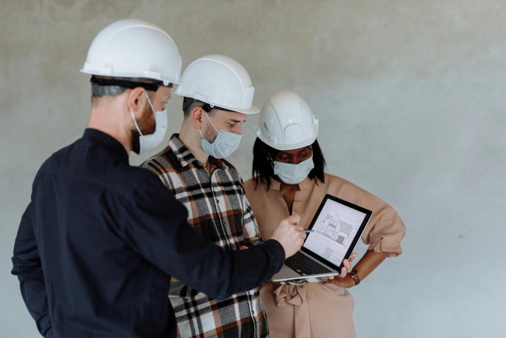 Group of diverse architects with safety gear examining building plans on a laptop.