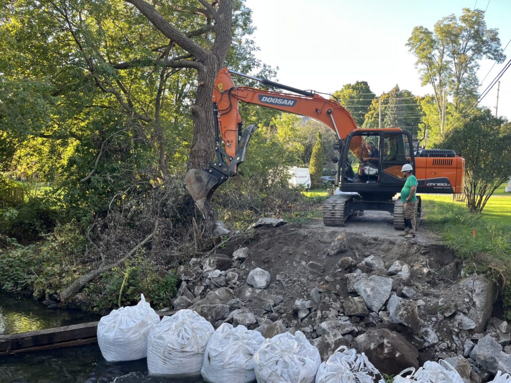 Excavator placing shoreline protection along a creek